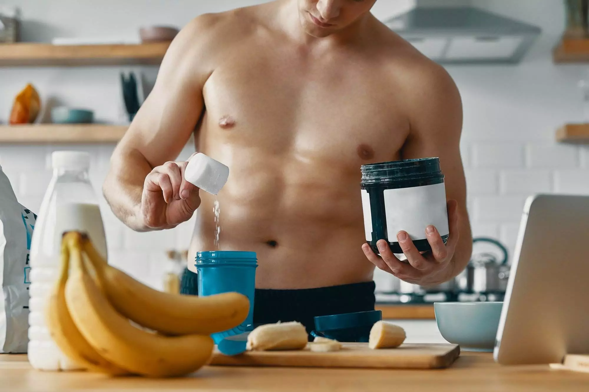 Handsome fit man preparing protein drink while standing at the kitchen
