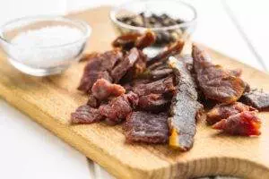 Beef jerky slices on wooden board with spices.