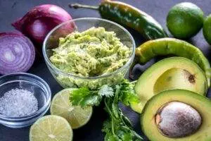 Fresh guacamole with ingredients on dark background