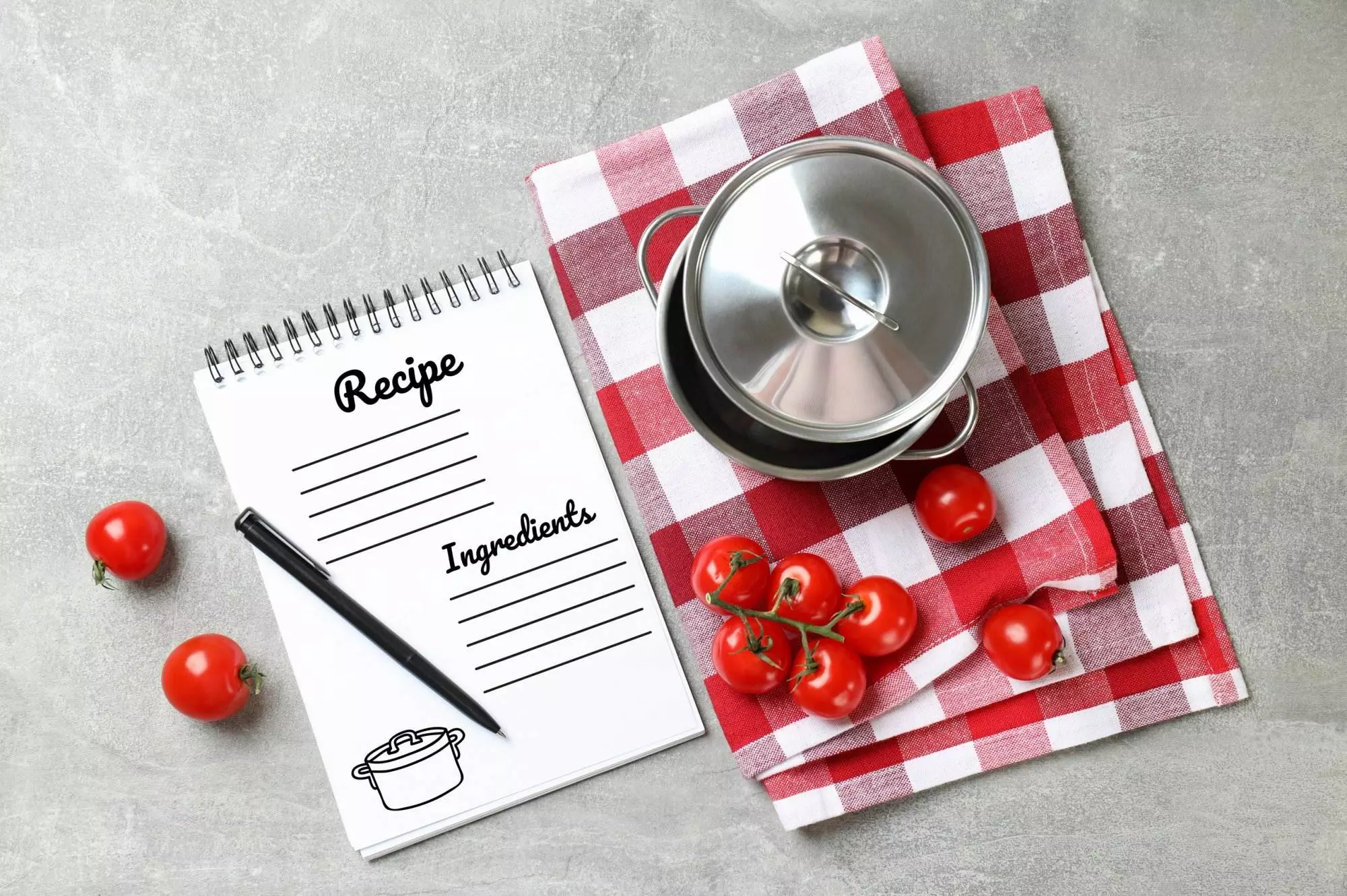 Recipe notepad, pot, tomatoes on kitchen table.