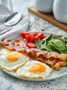 Keto low carb breakfast with Sunny-side up eggs with bacon, tomatoes, and spinach.