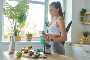 Woman preparing sports supplement in bright kitchen.