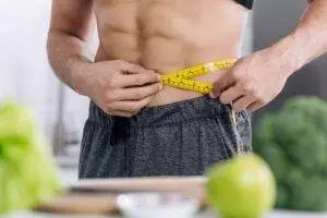 Man measuring waistline with tape measure near healthy food.