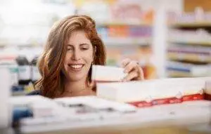 Woman finding supplement package on natural health store shelf.
