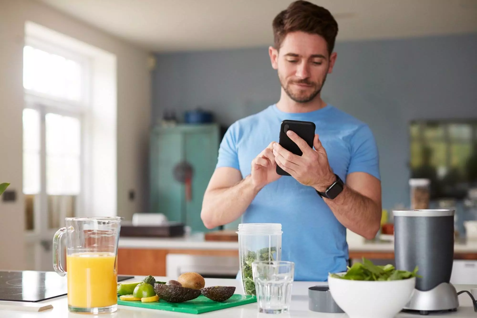 Man using smartphone fitness and diet app in kitchen with healthy food.