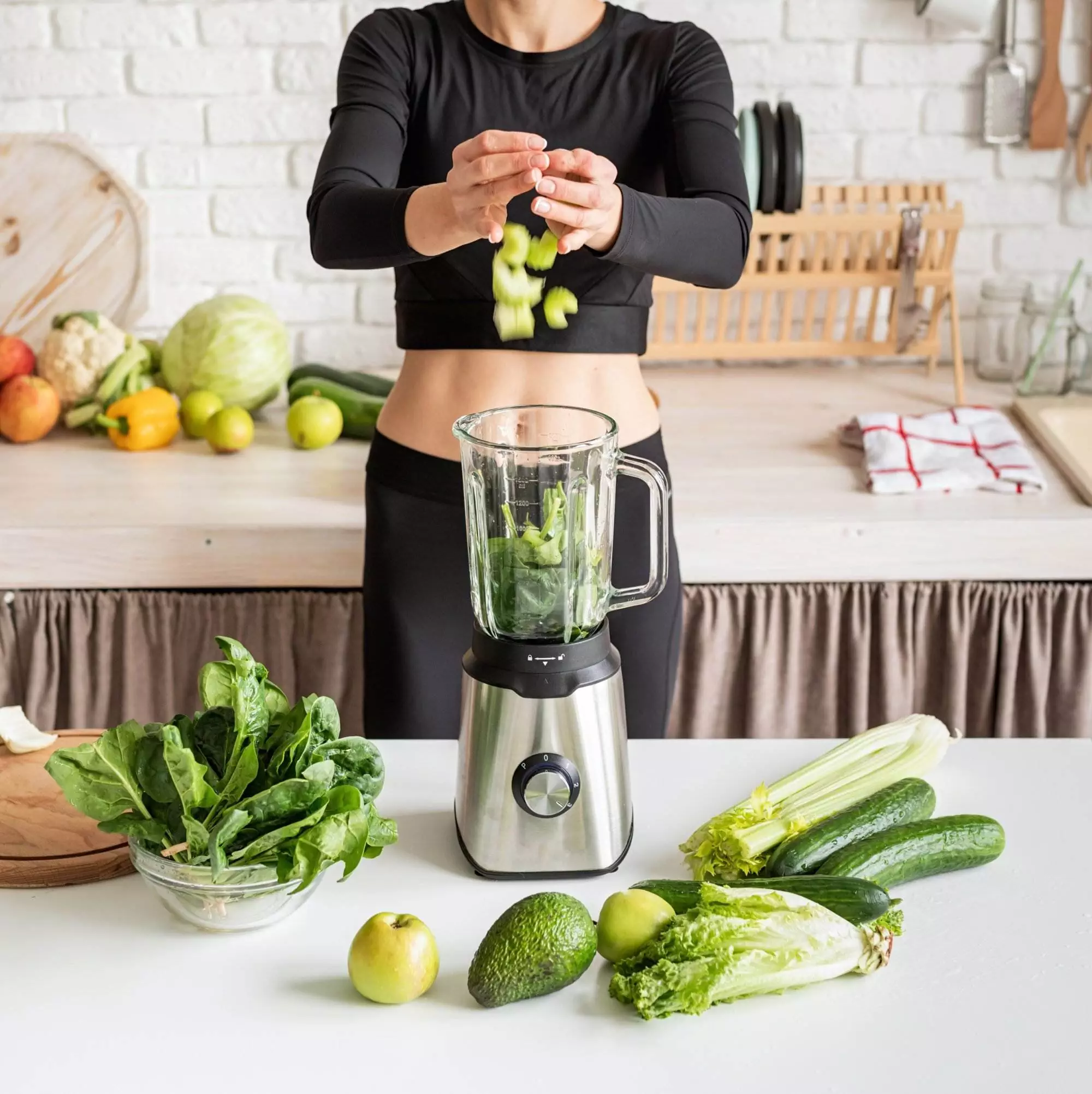 Woman making green smoothie with fresh vegetables.
