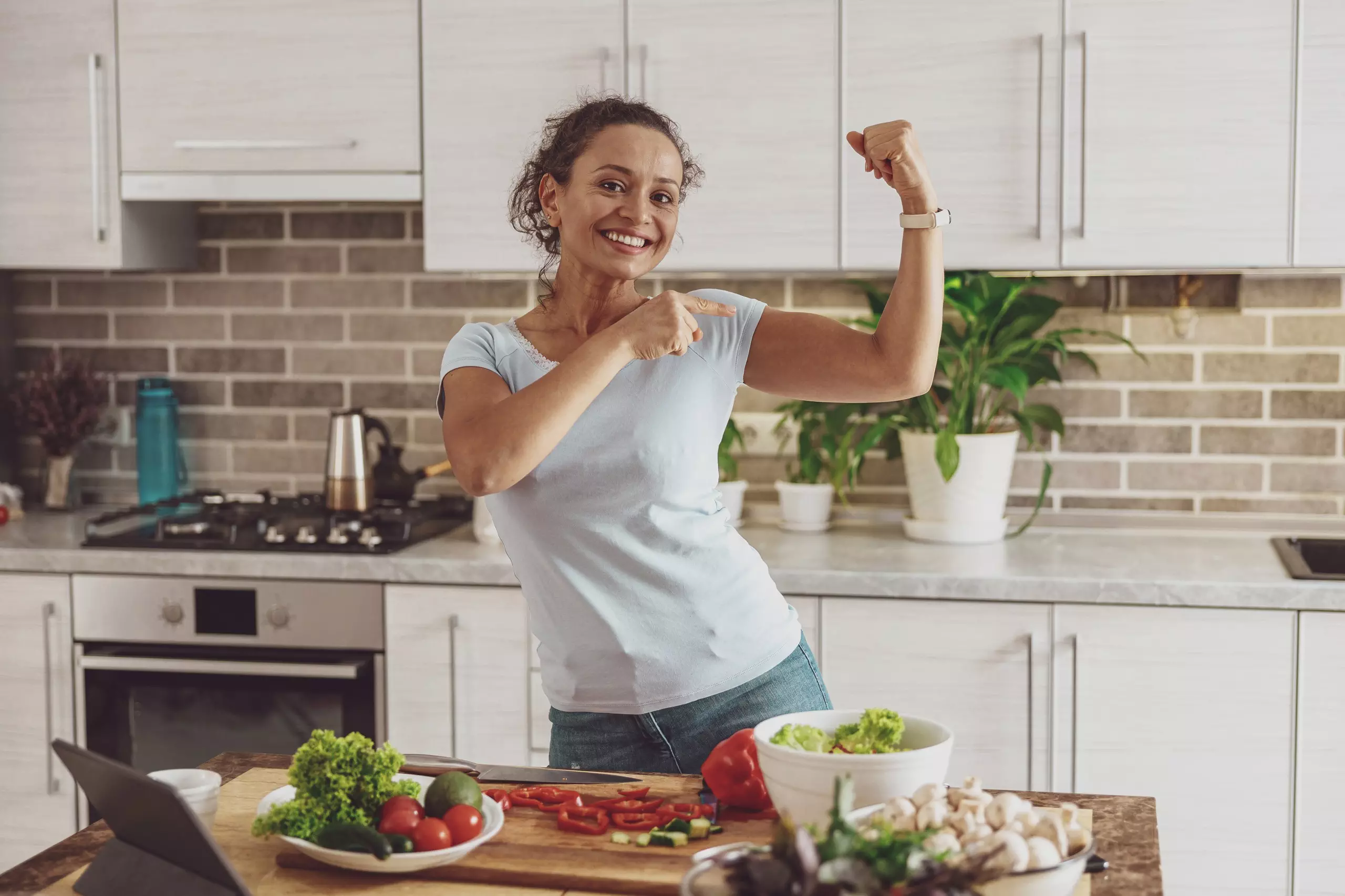 Woman flexing arm in healthy kitchen setting.