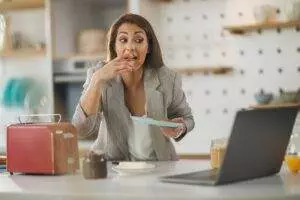 Woman eating toast while working on laptop.