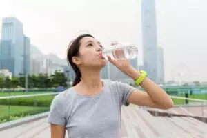 Woman drinking water in urban park setting.