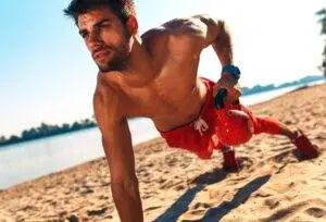Man doing fitness workout at a beach using kettlebell for push ups.