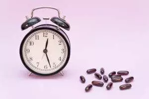 Vintage alarm clock and supplements on pink background.