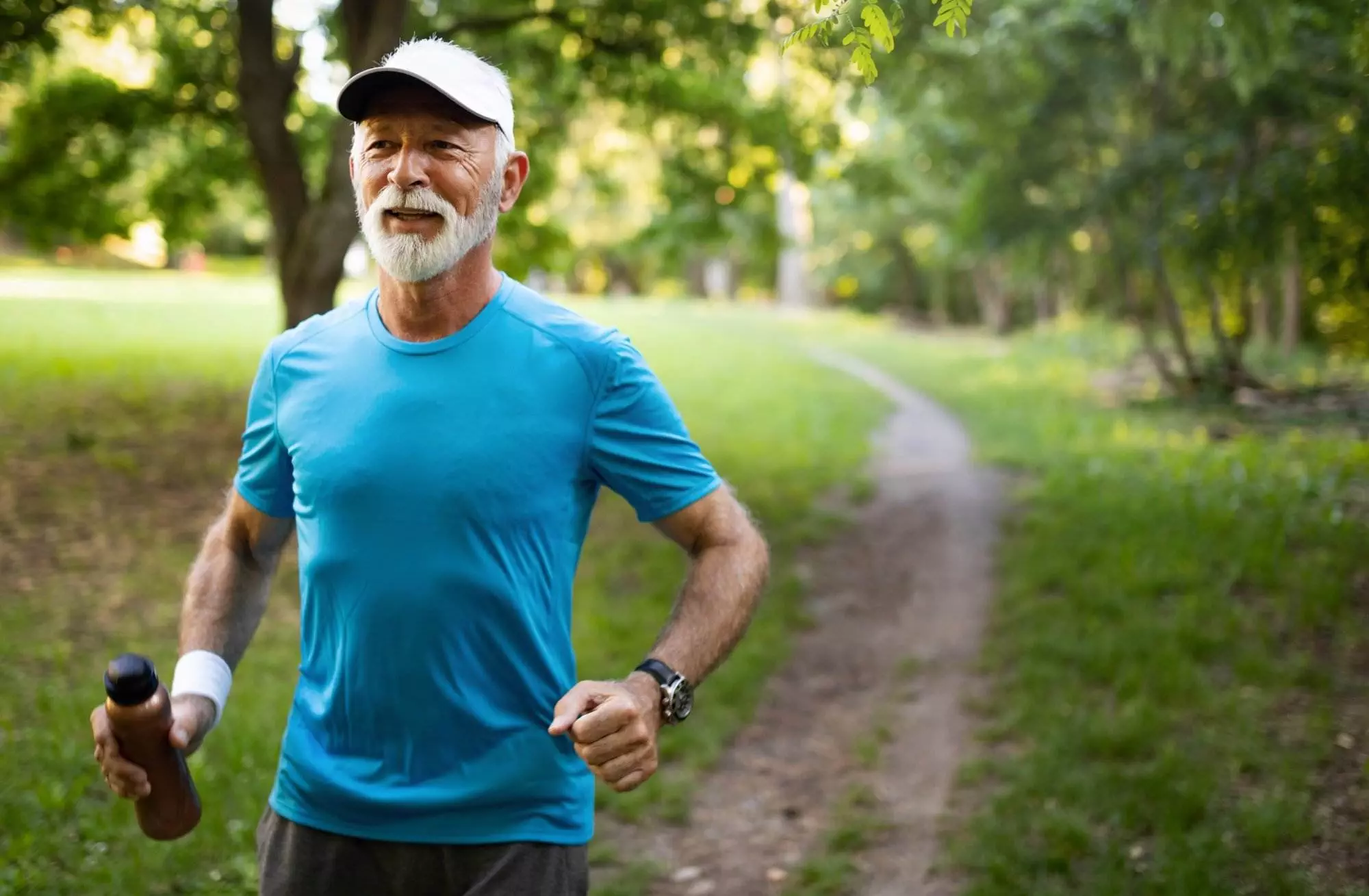 Senior man jogging in park with water bottle.