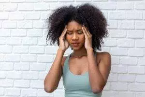 Woman with headache against white brick wall