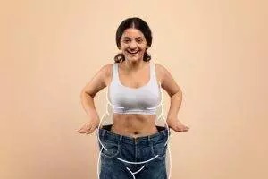 Happy woman showing weight loss in oversized jeans.