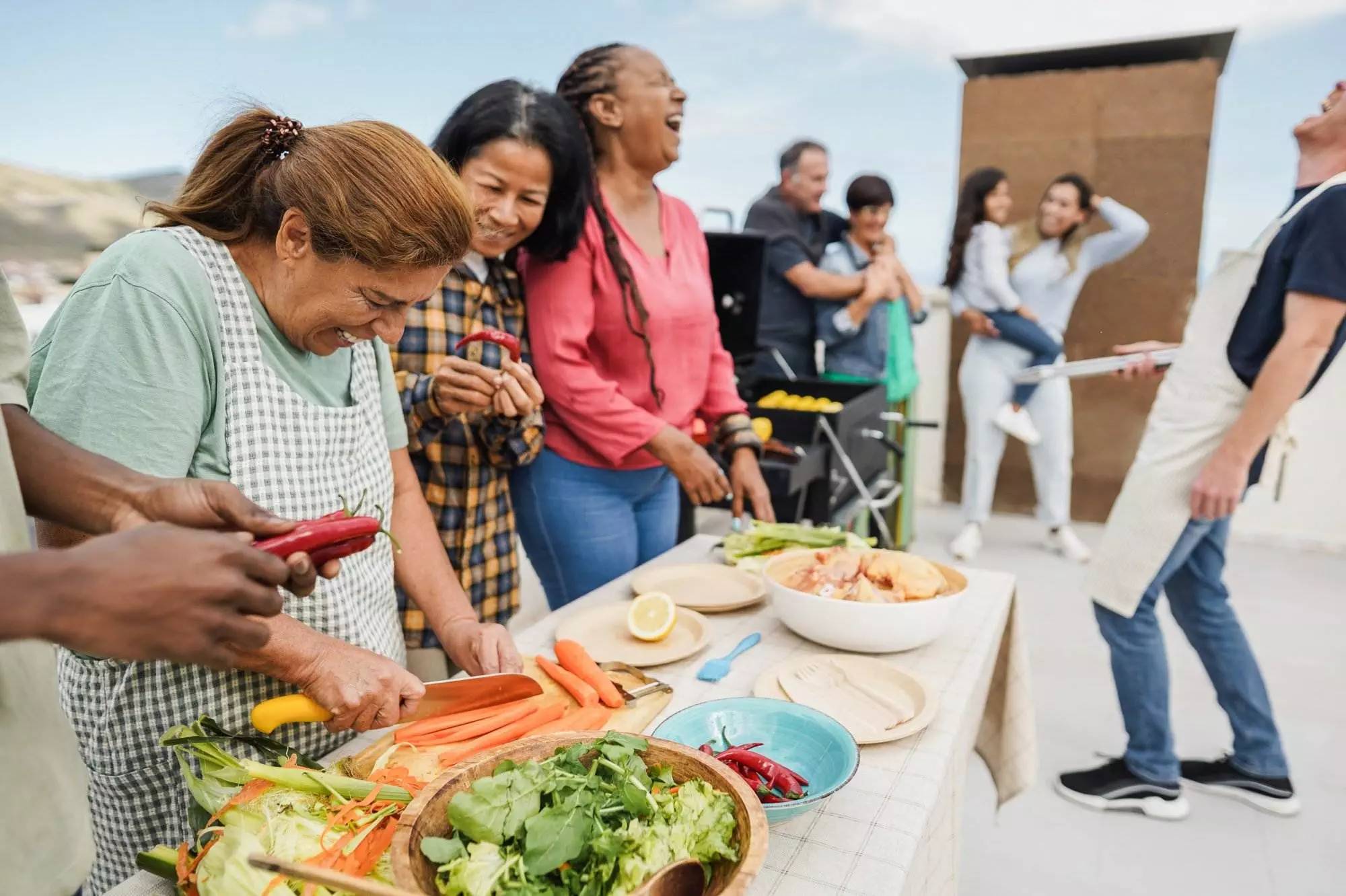 Diverse friends laughing and preparing food at outdoor party.