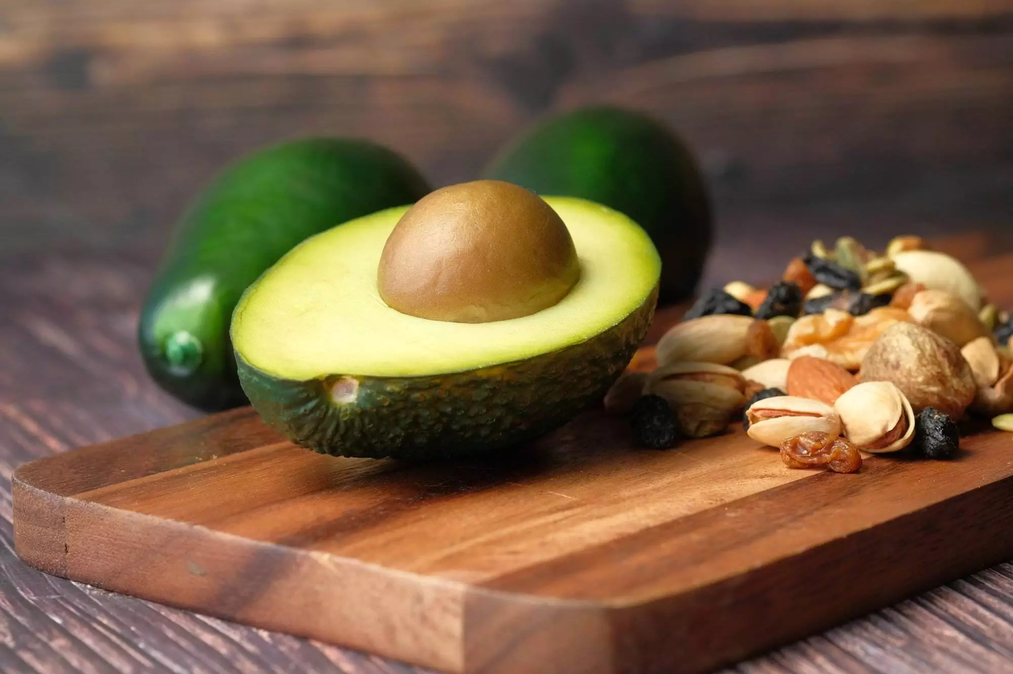 Halved avocado and mixed nuts on wooden board.