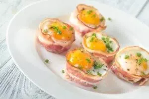 Bacon-wrapped eggs with chives on white plate.