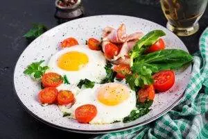 Fried eggs with tomatoes, spinach, and bacon on plate.