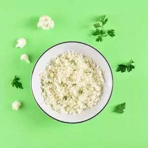 Cauliflower rice in a bowl with parsley on green background.