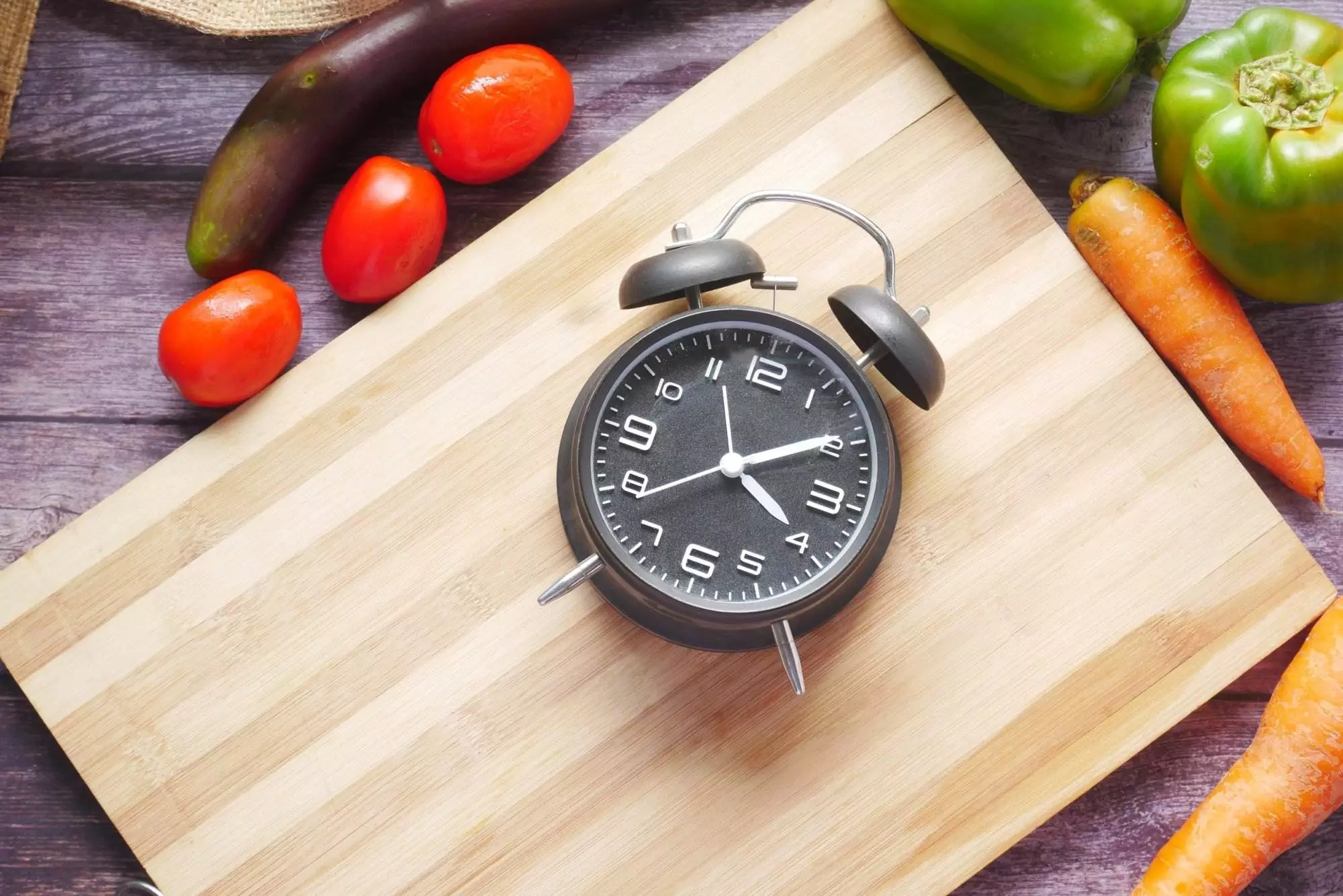 Alarm clock on cutting board with vegetables.