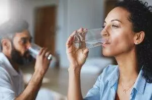 Two people drinking water from glasses indoors.