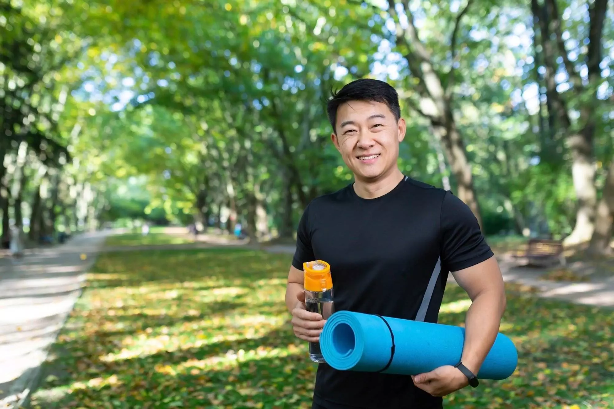 Man with yoga mat and water bottle in park fit and healthy