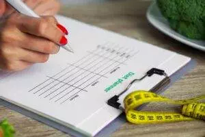 Writing diet plan with measuring tape nearby.
