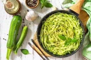 Healthy vegan food, low carb dish. Cooked zucchini noodles with basil and garlic on a rustic wooden table. Top view flat lay background.