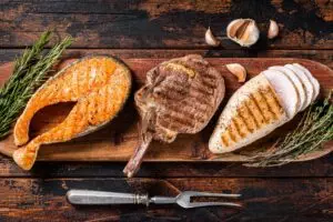 Barbecue grilled steaks - salmon, beef rib eye and turkey breast fillet on a wooden board.