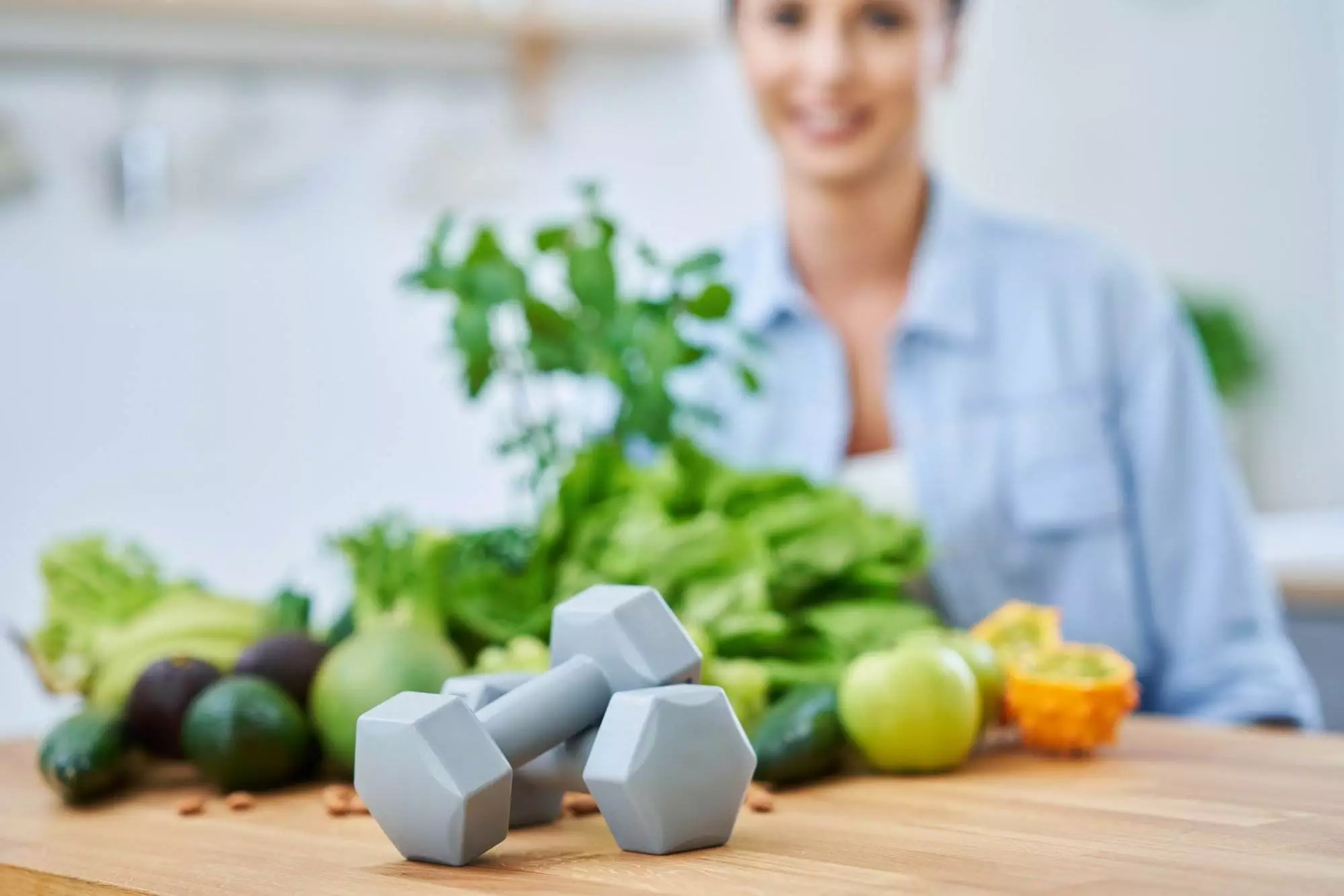 Woman with healthy food and dumbbells on table.
