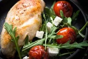 Grilled chicken breast with arugula and roasted tomatoes.