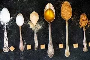 Spoons with sugar, honey, brown sugar on dark background.
