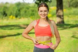 Healthy young Woman measuring waist with tape in park