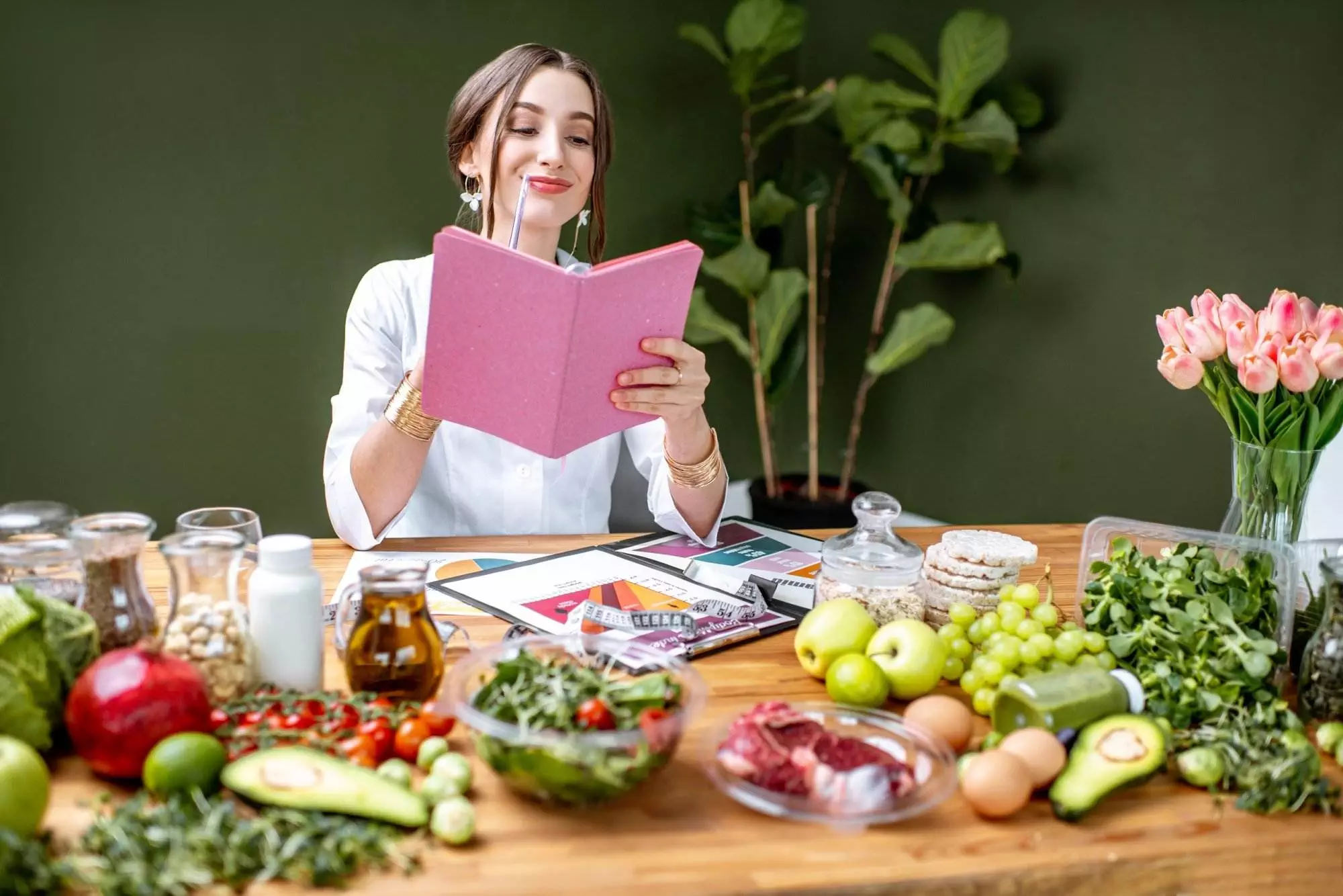 Woman reading recipe book amidst fresh groceries.