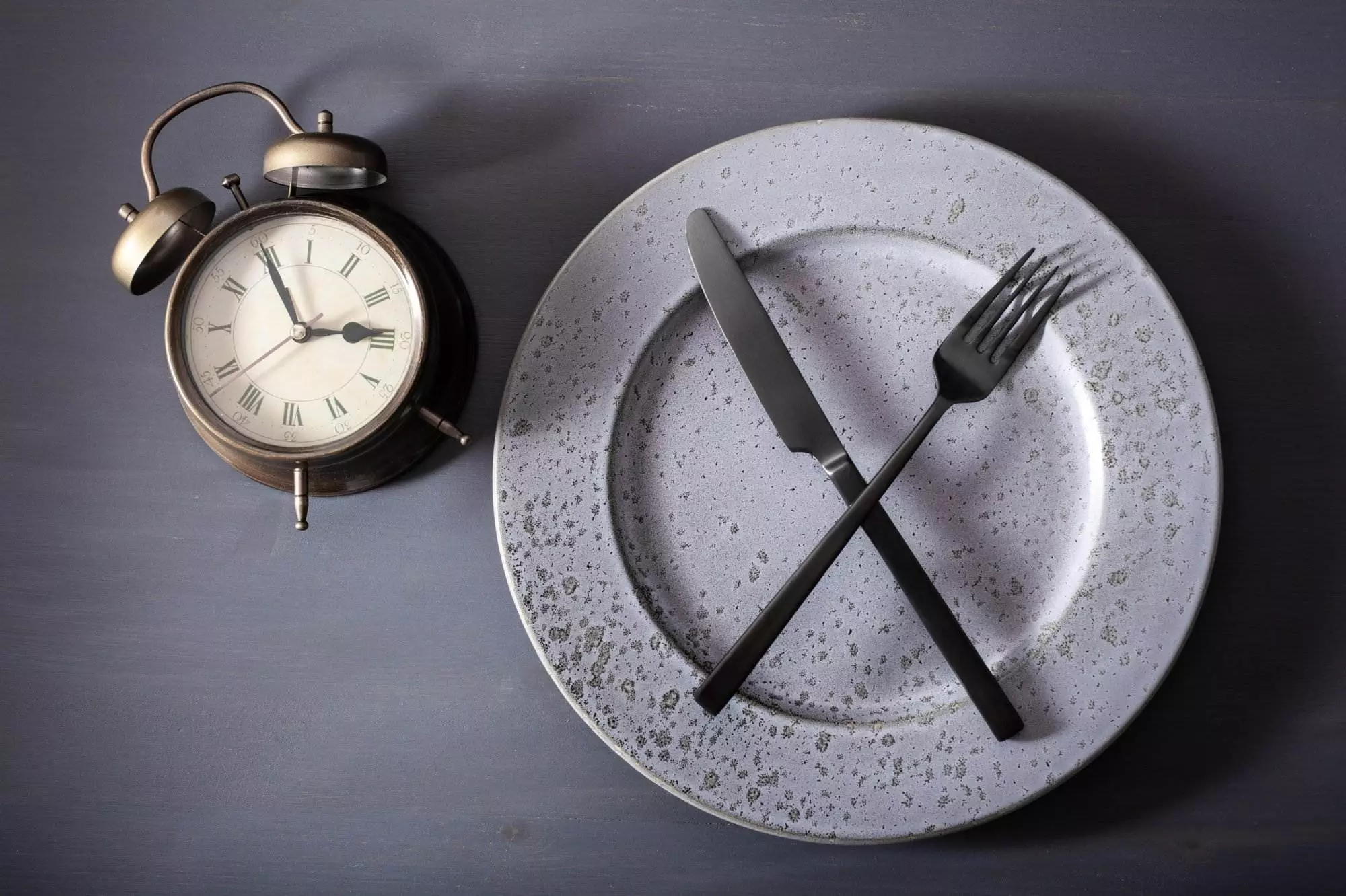 concept of intermittent fasting, ketogenic diet, weight loss. fork and knife crossed on a plate and alarm clock