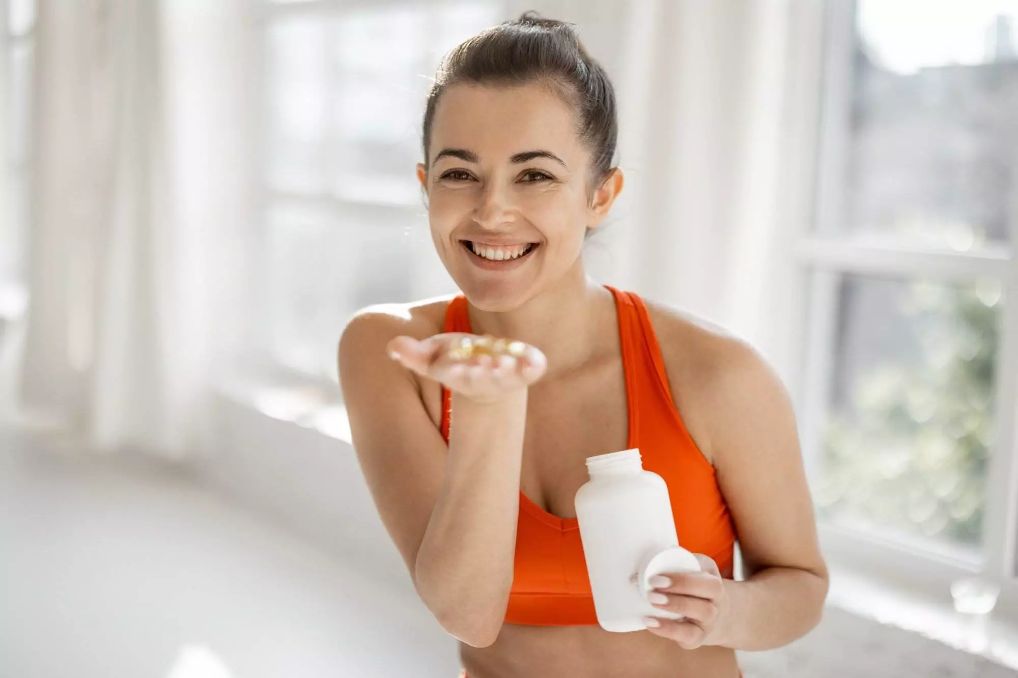 Portrait of a cheerful woman taking supplements or vitamins in the form of capsules after training in the gym. Concept of additional nutrition during training