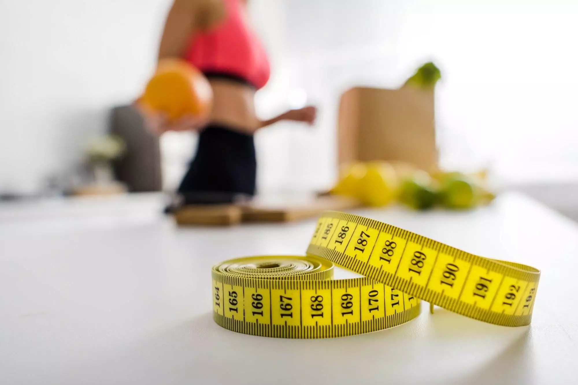 Measuring tape with person holding fruit for weight loss.