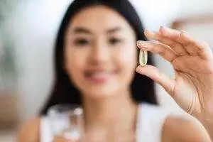 Woman holding omega-3 supplement capsule.