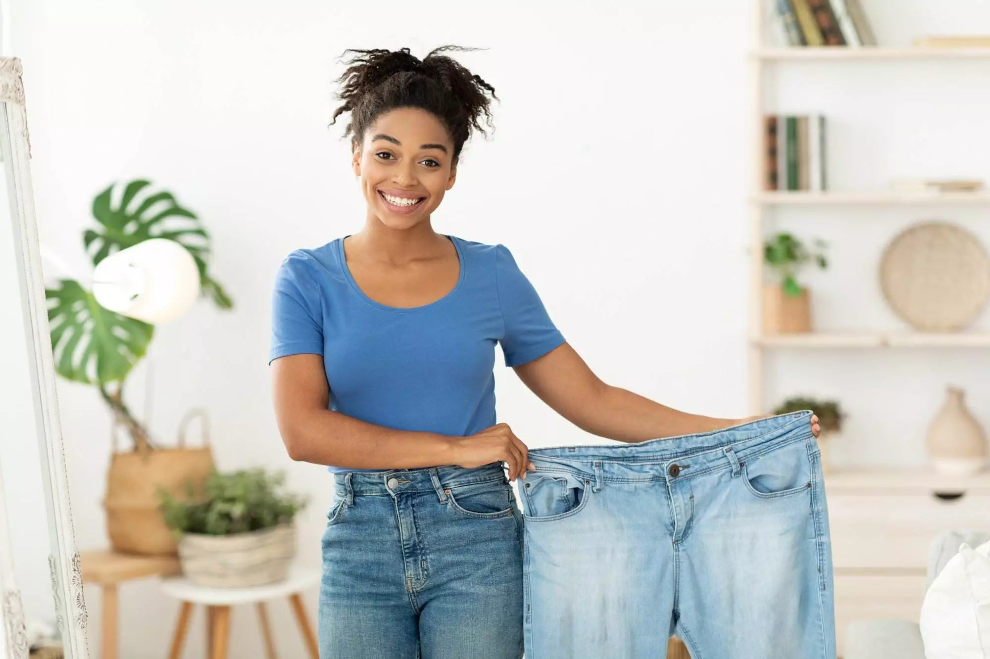 Woman showing weight loss by holding large jeans.