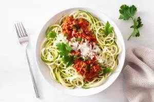 Zucchini noodles with tomato sauce and cheese garnish.