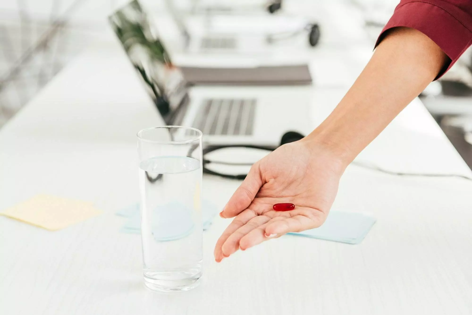 Business professional holding supplement near glass of water and laptop in office