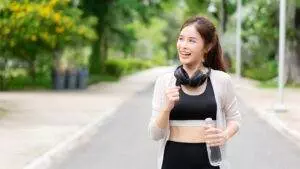 Healthy Asian Woman walking with headphones and water bottle.