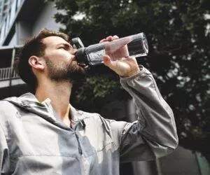 Man drinking water from clear bottle outdoors; Hydration