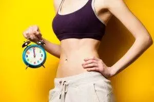Woman holding alarm clock, fitness time concept.