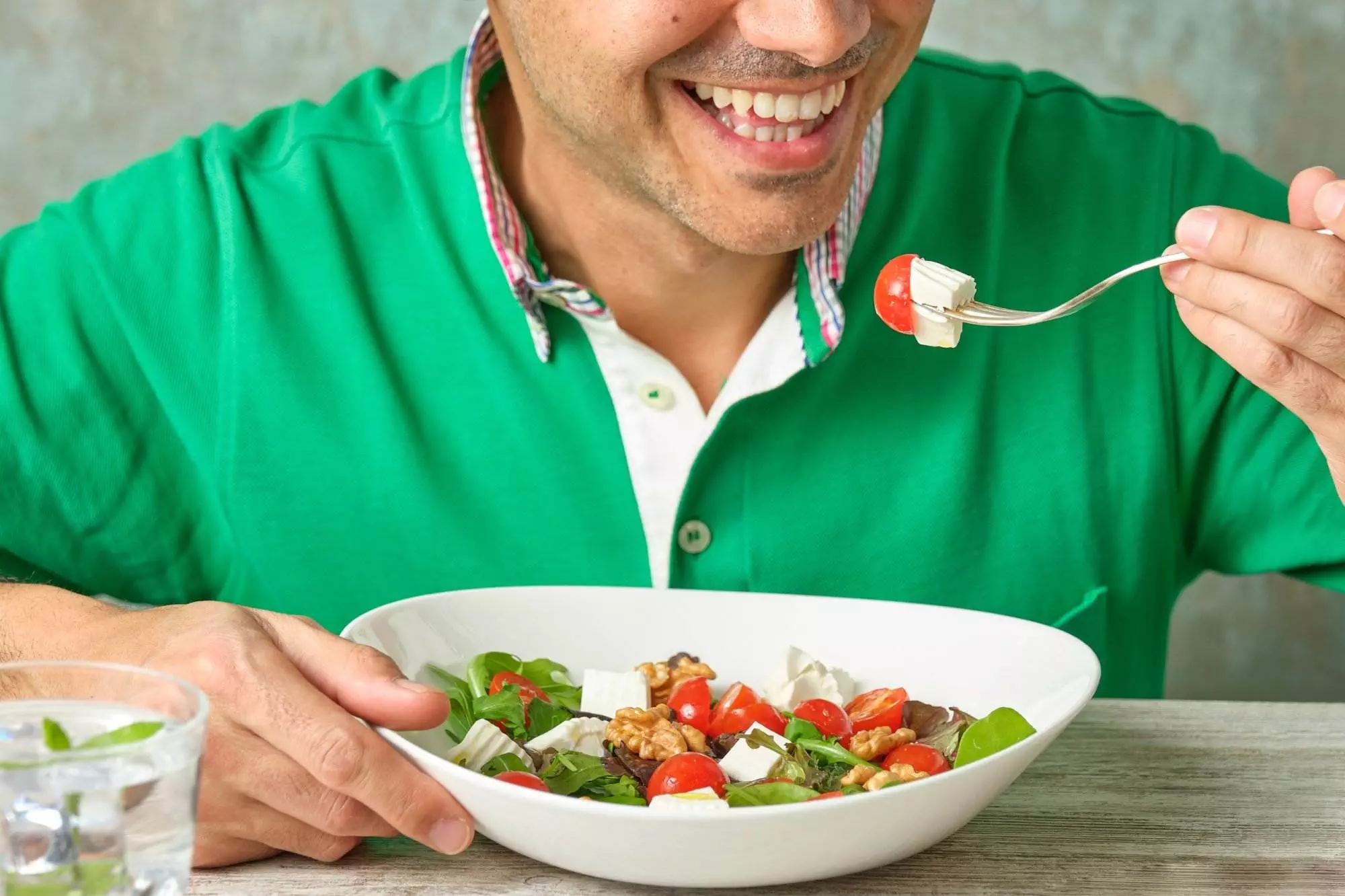 Man smiling while eating fresh salad.