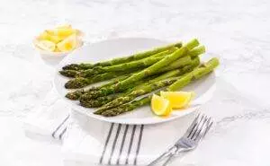 Fresh asparagus with lemon slices on white plate.