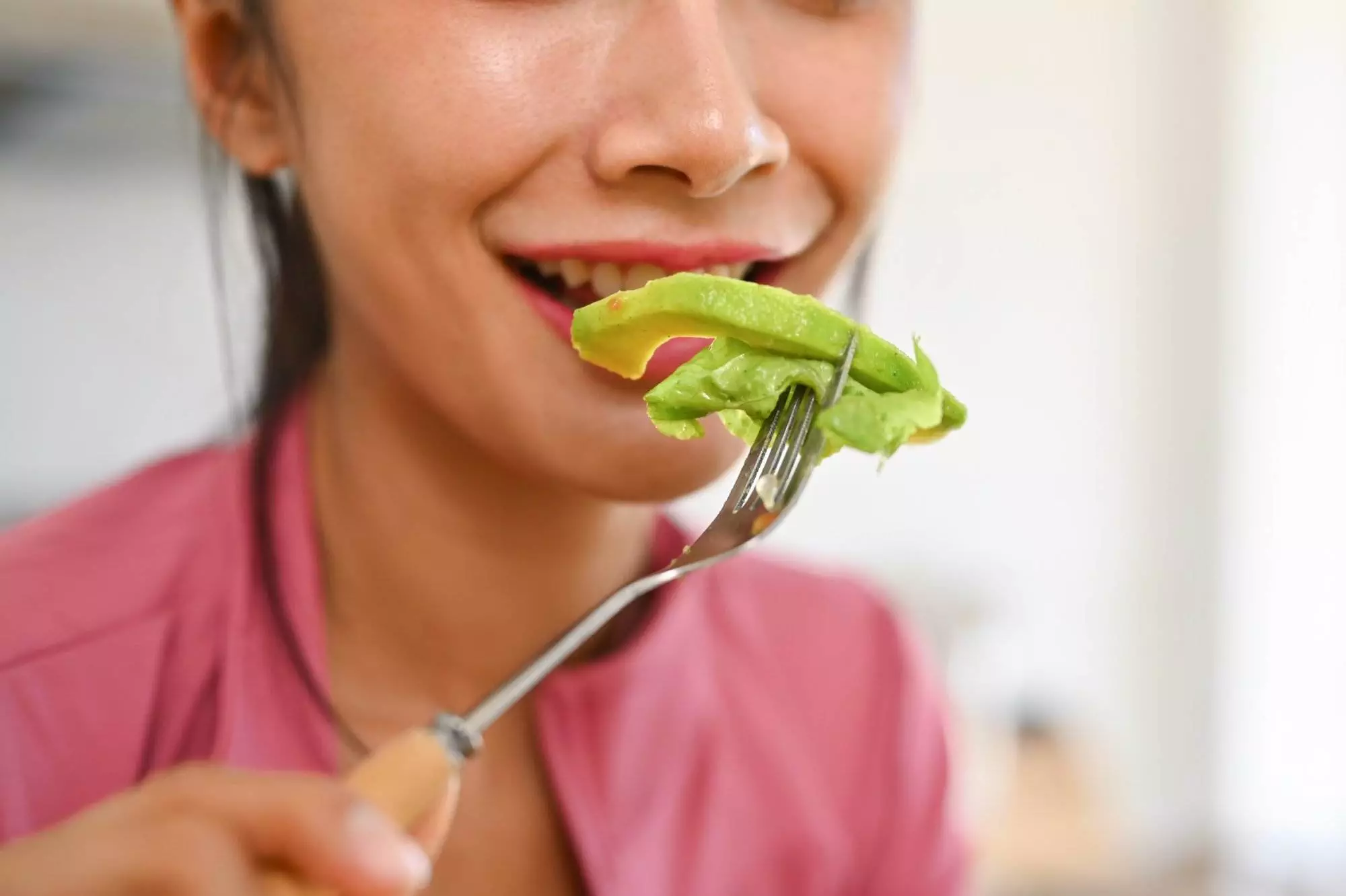 Woman eating fresh avocado on fork.