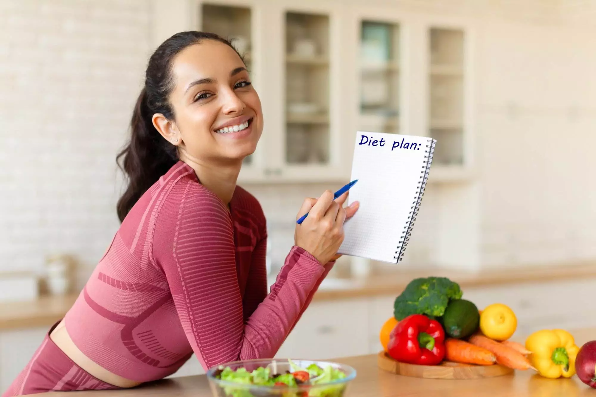 Woman smiling, writing on diet plan with fresh vegetables.