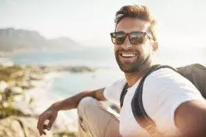 Man smiling outdoors with sunglasses, coastal background.