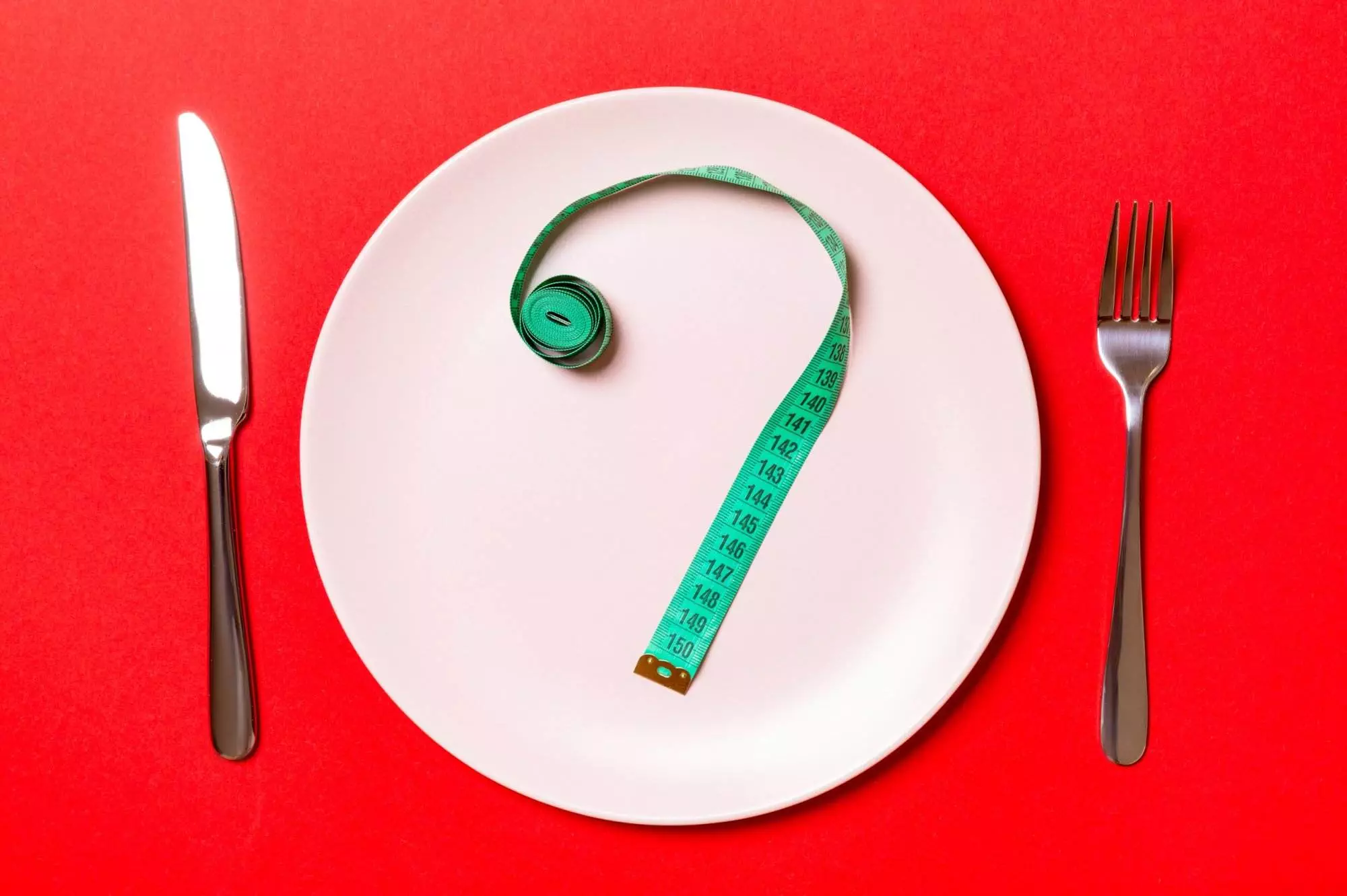 Measuring tape on plate, diet concept, red background.